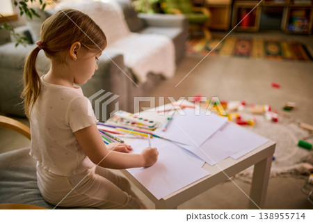 Little girl drawing with pencils at small table in cozy home interior. Little girl drawing with pencils at small table in cozy home interior. 138955714