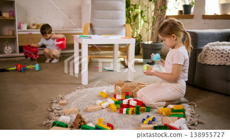 Little girl playing with toys while boy in background making mess in living room. Little girl playing with toys while boy in background making mess in living room. 138955727