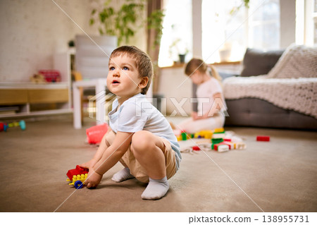 Little boy squatting on floor playing with colorful toy car in living room. 138955731