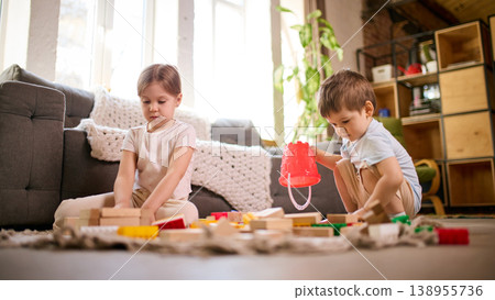 Two children playing with wooden and plastic blocks together on living room floor. Two children playing with wooden and plastic blocks together on living room floor. 138955736