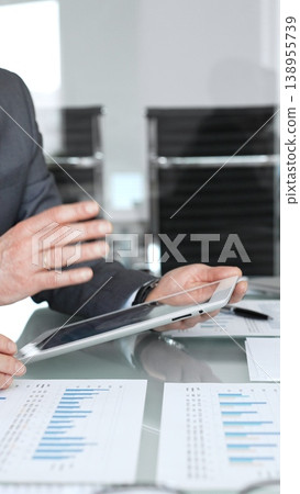 Business professionals analyzing financial data on a digital tablet and printed charts, collaborating on strategy and planning during a corporate meeting in an office setting 138955739