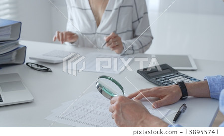 Accounting professionals analyzing financial documents, checking spreadsheet details with calculator and magnifying glass. Audit and taxes in business Accounting professionals analyzing financial documents, checking spreadsheet details with calculator and magnifying glass. Audit and taxes in business 138955741