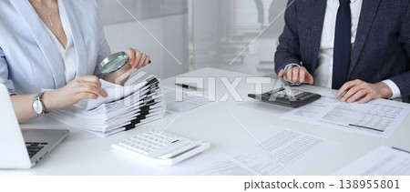 Professional auditors reviewing financial paperwork, using magnifying glass and calculator while analyzing business documents for detailed inspection and accounting compliance. Audit and taxes Professional auditors reviewing financial paperwork, using magnifying glass and calculator while analyzing business documents for detailed inspection and accounting compliance. Audit and taxes 138955801