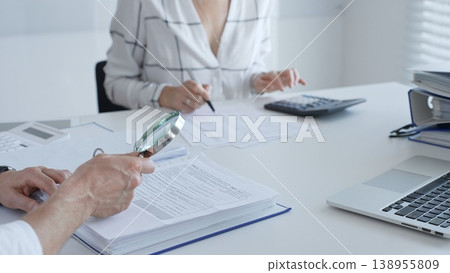 Two professional accountants colleagues are working together, using a magnifying glass and a calculators, to audit financial reports in office. Audit and taxes in business 138955809
