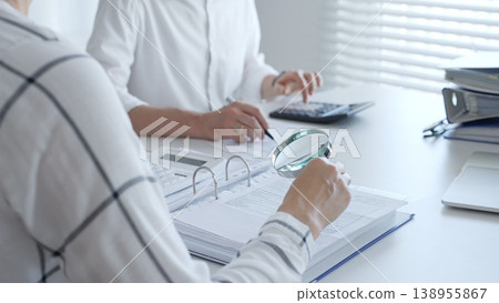 Team of accountants are working together, using a magnifying glass and a calculator, to audit financial reports in office. Audit and taxes in business 138955867