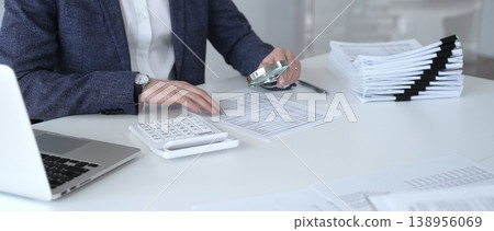 Business professional inspecting financial reports with a magnifying glass and calculator, auditing tax documents and data. Audit and taxes Business professional inspecting financial reports with a magnifying glass and calculator, auditing tax documents and data. Audit and taxes 138956069