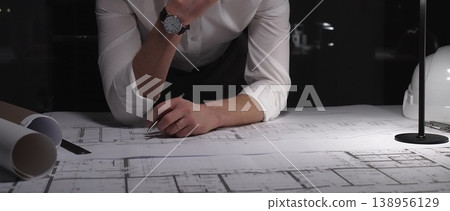 Architect carefully planning building blueprint, thinking about engineering design and development at late night workstation. Business and architect people concept Architect carefully planning building blueprint, thinking about engineering design and development at late night workstation. Business and architect people concept 138956129