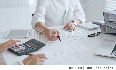 Two accountants collaborating in a well lit office, analyzing financial data and preparing reports with calculators and pens. Audit and taxes in business Two accountants collaborating in a well lit office, analyzing financial data and preparing reports with calculators and pens. Audit and taxes in business 138956163