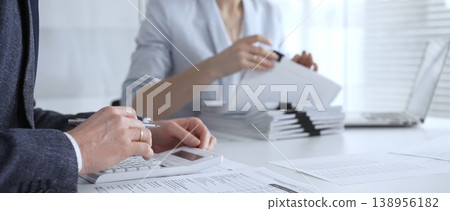 Business professionals working on financial reports, calculating taxes and managing paperwork at an office desk, collaborating on accounting tasks and corporate documentation. Audit and taxes Business professionals working on financial reports, calculating taxes and managing paperwork at an office desk, collaborating on accounting tasks and corporate documentation. Audit and taxes 138956182