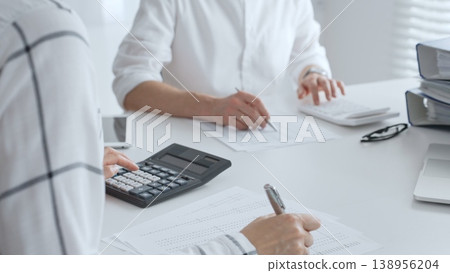 Unrecognizable accountants working together in a well lit office, analyzing financial data and preparing reports with calculators and pens. Audit and taxes in business Unrecognizable accountants working together in a well lit office, analyzing financial data and preparing reports with calculators and pens. Audit and taxes in business 138956204