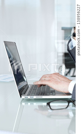 Businessman in a modern office intently typing on a laptop, deeply focused and analyzing data to develop solutions and strategies for projects and corporate challenges Businessman in a modern office intently typing on a laptop, deeply focused and analyzing data to develop solutions and strategies for projects and corporate challenges 138956227
