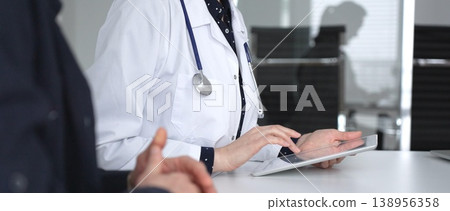 Female doctor consulting patient man using digital tablet, discussing medical records in modern clinic office, healthcare technology. Medicine, healthcare and science concept 138956358