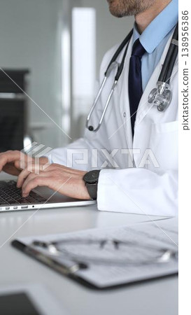 Medical professional typing on laptop, reviewing patient data, consulting online, using telehealth technology. Medicine, healthcare and science concept 138956386