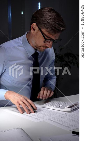 Accountant working late night in office, calculating finance data and economy statistics in a blue shirt with a tie. Audit and taxes in business 138956428