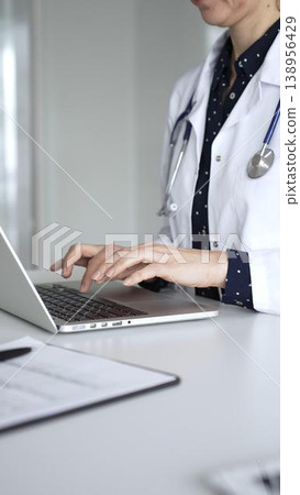 Professional doctor reviewing electronic medical records and typing information on laptop during remote consultation. Medicine, healthcare and science concept 138956429