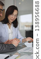 Diverse business professionals collaborating on a project, analyzing data and reviewing documents on a digital device during an important office meeting. Vertical composition 138956688