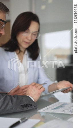 Diverse business professionals collaborating on a project, analyzing data and reviewing documents on a digital device during an important office meeting. Vertical composition 138956688