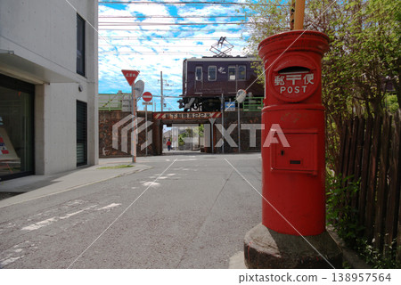 A scene featuring a retro red, round mailbox from the Showa era and the Hankyu Railway running on an elevated track. A scene featuring a retro red, round mailbox from the Showa era and the Hankyu Railway running on an elevated track. 138957564