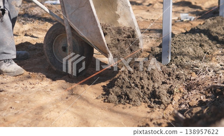 Man Carries Mixture Across Uneven Terrain. Team Moves Building Supplies While Dust Fills Air. Construction Workers Transport Mortar Over Rugged Ground As Dust Rises In Sunlight Man Carries Mixture Across Uneven Terrain. Team Moves Building Supplies While Dust Fills Air. Construction Workers Transport Mortar Over Rugged Ground As Dust Rises In Sunlight 138957622