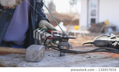 Field Fabricator Grinding Metal Outdoors On Makeshift Bench, Sparks Scattering In Daylight, Hands And Gloves Visible, Rugged Site Atmosphere With Portable Tools And Focused Finishing Work. Field Fabricator Grinding Metal Outdoors On Makeshift Bench, Sparks Scattering In Daylight, Hands And Gloves Visible, Rugged Site Atmosphere With Portable Tools And Focused Finishing Work. 138957658