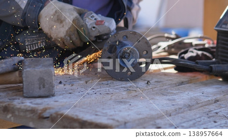 Closeup Construction Worker Grinding Flange, Sparks Fly Against Scaffold Backdrop, Heavy Gloves And Safety Gear, Outdoor Repair On Platform With Concrete And Timber Nearby Closeup Construction Worker Grinding Flange, Sparks Fly Against Scaffold Backdrop, Heavy Gloves And Safety Gear, Outdoor Repair On Platform With Concrete And Timber Nearby 138957664
