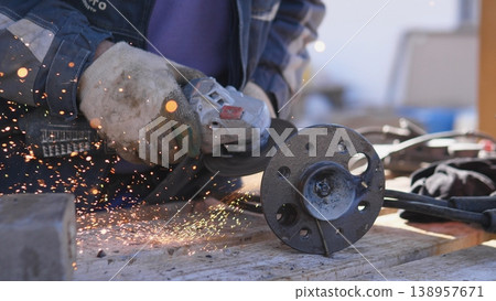 Closeup Hands Grinding Metal Flange, Fabricator Smoothing Edge On Steel Component, Heavy Gloves, Power Grinder Throwing Bright Sparks Over Wooden Bench, Workshop Tools Scattered Closeup Hands Grinding Metal Flange, Fabricator Smoothing Edge On Steel Component, Heavy Gloves, Power Grinder Throwing Bright Sparks Over Wooden Bench, Workshop Tools Scattered 138957671