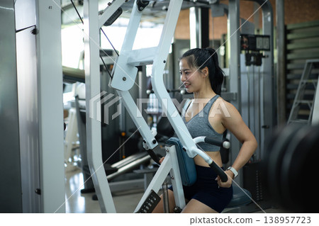 Athletic woman exercising back muscles on seated Row Machine in gym Athletic woman exercising back muscles on seated Row Machine in gym 138957723