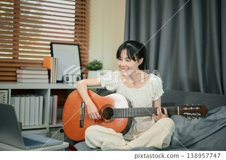 Young woman Practice playing the guitar with online exercises Young woman Practice playing the guitar with online exercises 138957747