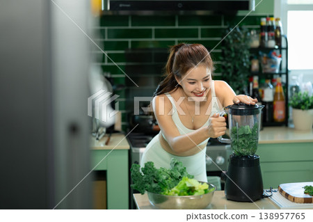 Smiling woman using blender to make fresh green smoothie 138957765