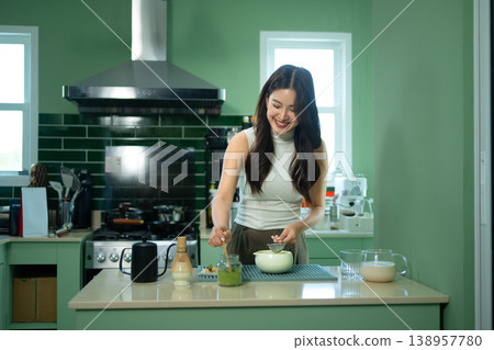 Smiling woman whisking matcha in modern green kitchen during calm morning routine 138957780