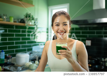 Smiling fit woman holding green juice in kitchen Smiling fit woman holding green juice in kitchen 138957797