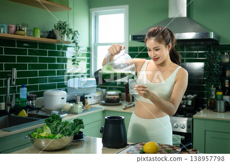 Sporty woman pouring green smoothie in modern kitchen 138957798
