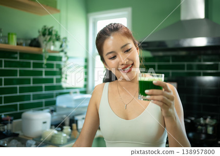 Smiling fit woman holding green juice in kitchen Smiling fit woman holding green juice in kitchen 138957800