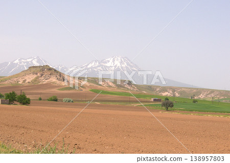 Mount Hasan Volcano Cappadocia Landscape. Majestic snow-capped Mount Hasan peaks over green spring fields in Cappadocia, Turkey. Mount Hasan Volcano Cappadocia Landscape. Majestic snow-capped Mount Hasan peaks over green spring fields in Cappadocia, Turkey. 138957803