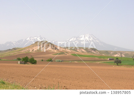 Mount Hasan Volcano Cappadocia Landscape. Majestic snow-capped Mount Hasan peaks over green spring fields in Cappadocia, Turkey. Mount Hasan Volcano Cappadocia Landscape. Majestic snow-capped Mount Hasan peaks over green spring fields in Cappadocia, Turkey. 138957805