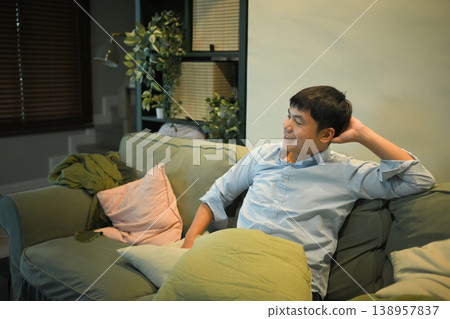 Smiling man relaxing on a sofa in cozy living room with warm indoor lighting 138957837