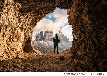 Male tourist standing at front of rock cave of Grotta delle Tre Cime with mountain peak in Dolomites, Italy Male tourist standing at front of rock cave of Grotta delle Tre Cime with mountain peak in Dolomites, Italy 138958087