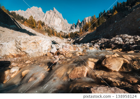 Alpine landscape of Dolomites rugged mountain and water flows in autumn larch forest Alpine landscape of Dolomites rugged mountain and water flows in autumn larch forest 138958124