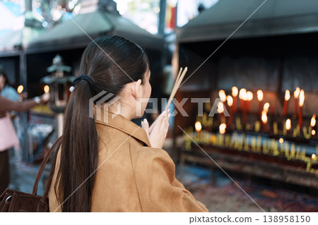 Asian woman praying with incense sticks at buddhist temple 138958150