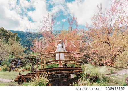 Relaxed woman standing on wooden bridge in Wild Himalayan Cherry blooming Relaxed woman standing on wooden bridge in Wild Himalayan Cherry blooming 138958162