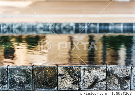Infinity pool edge with dark stone tiles and water reflection 138958268