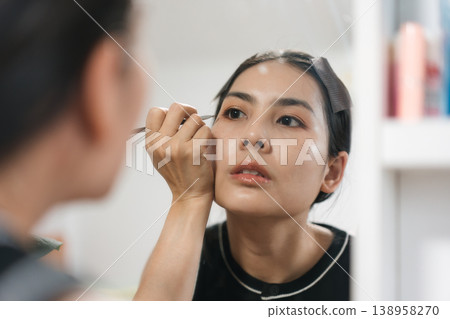 Beautiful Thai woman applying makeup with eye liner, eyebrow pencil in front of mirror. Lifestyle concept for cosmetics and self care Beautiful Thai woman applying makeup with eye liner, eyebrow pencil in front of mirror. Lifestyle concept for cosmetics and self care 138958270