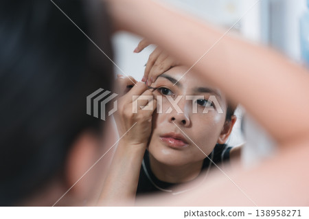 Beautiful Thai woman applying makeup with eye liner, eyebrow pencil in front of mirror. Lifestyle concept for cosmetics and self care Beautiful Thai woman applying makeup with eye liner, eyebrow pencil in front of mirror. Lifestyle concept for cosmetics and self care 138958271