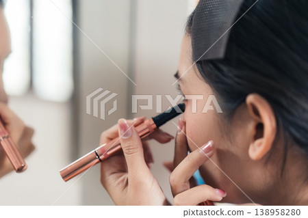 Beautiful Thai woman applying makeup with eye liner, eyebrow pencil in front of mirror. Lifestyle concept for cosmetics and self care 138958280