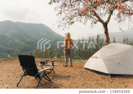 Solo man camping with tent and coffee overlooking mountain valley in countryside Solo man camping with tent and coffee overlooking mountain valley in countryside 138958308