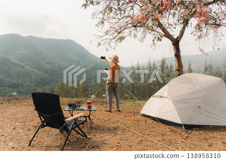 Man camping with coffee and selfie with smartphone at scenic mountain valley Man camping with coffee and selfie with smartphone at scenic mountain valley 138958310