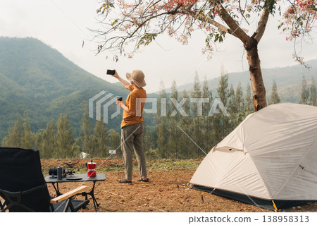 Man camping with coffee and selfie with smartphone at scenic mountain valley Man camping with coffee and selfie with smartphone at scenic mountain valley 138958313