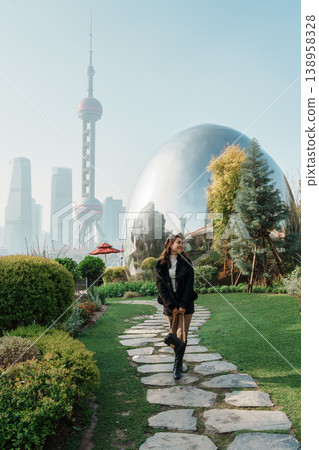 Stylish female tourist walking on Shanghai park with iconic Oriental Pearl Tower and skyscraper in North Bund Green Land Stylish female tourist walking on Shanghai park with iconic Oriental Pearl Tower and skyscraper in North Bund Green Land 138958328
