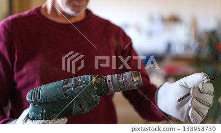 Artisan wearing gloves inserting drill bit into power tool Artisan wearing gloves inserting drill bit into power tool 138958730