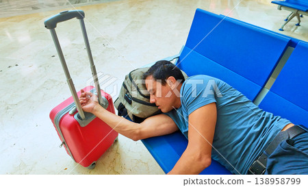 Man sleeping on blue terminal benches with backpack and luggage Man sleeping on blue terminal benches with backpack and luggage 138958799